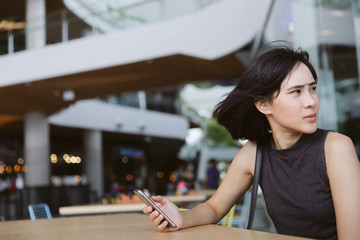 Young Asian Girl using mobile phone to connect internet wifi to send the sms message in the windy day.