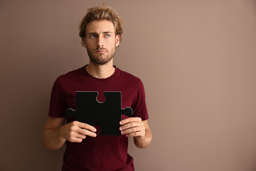 Thoughtful young man with piece of jigsaw puzzle on color background