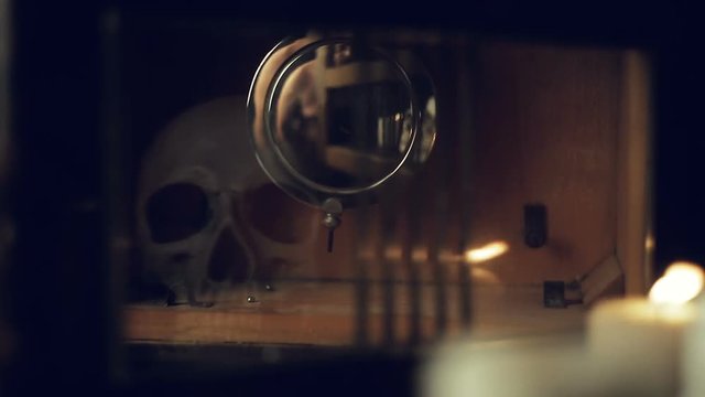 reflection of the skull and candles in the pendulum of an old clock