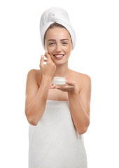 Beautiful young woman wrapped in towel holding jar of cream on white background