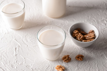 Glass of tasty milk and bowl with walnuts on white table