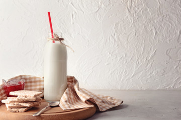 Composition with bottle of tasty milk, cookies and jam on wooden board