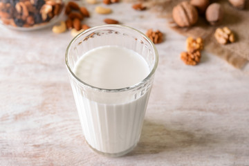 Glass of tasty milk and nuts on light table