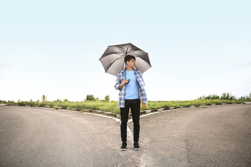 Young man with umbrella standing at crossroads. Concept of choice