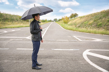 Young man with umbrella standing at crossroads. Concept of choice