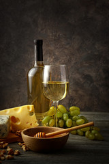 Glass and bottle of white wine with snacks and ripe grapes on wooden table