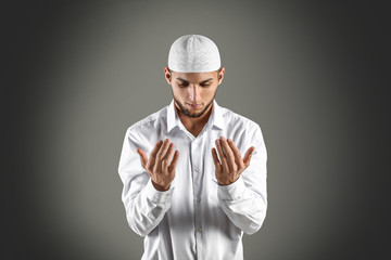 Young Muslim man praying on dark background