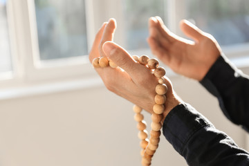 Young Muslim man with rosary beads praying at home, closeup