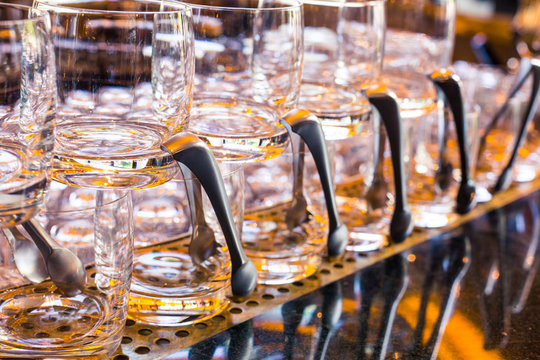 Transparent glasses for alcoholic beverages stand on the bar with a spatula. Yellow lights on the bar, the table reflects the glasses. Service in a restaurant or bar