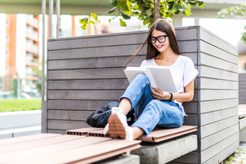 Portrait of pleased brunette woman in eyeglasses sitting on bench and reading book in park