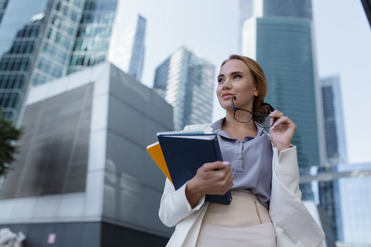 Beautiful young woman with folders and documents in her hands standing among the skyscrapers of the modern business center - Powered by Adobe