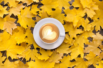 Autumn and november mood background. A cup of coffee with cappuccino and yellow maple leaves on old...