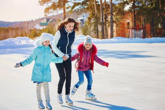 A group of three girls on a winter skating rink. Roll and laugh. Skating rink in nature.
