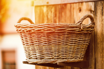 Fototapeta premium Big hand made basket in the light of evening sun placed near brown wooden wall