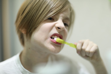 School boy with stylish haircut brushing his teeth in front of the mirror