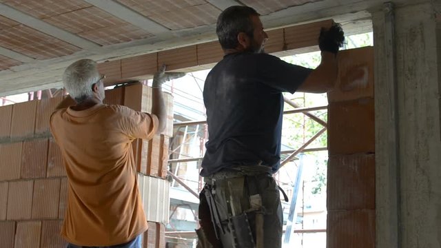 Two masons place the architrave on the doorway of the wall under construction
