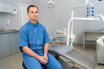 Fototapeta premium handsome young dentist sitting in dentist office and looking at camera