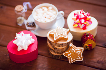Cup of chocolate with marshmallow, gingerbread cookies, gifts and beautiful Christmas decorations on the wooden background. Flat lay, top view, space for a text.