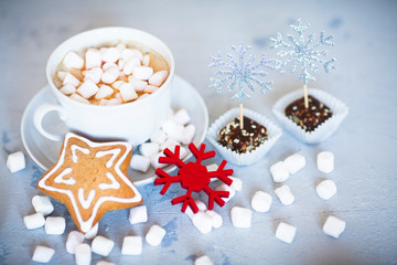 Hot coffee with marshmallows and gingerbread cookies on the light gray background. Beautiful Christmas decorations with gifts and sweets. Space for a text. Close up.