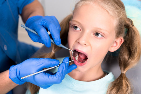 cropped shot of dentist with tools examining teeth of little child