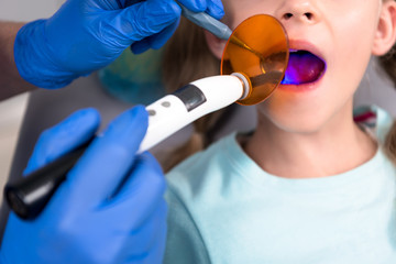 Naklejka premium cropped shot of dentist performing dental curing procedure for little child