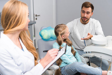 Fototapeta premium female dentist with clipboard talking to little child and her father