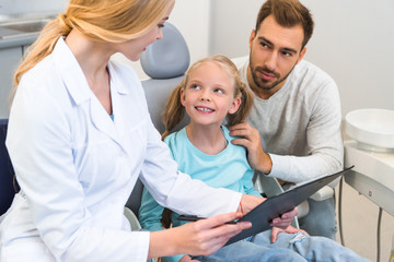 Obraz premium young female dentist showing clipboard with diagnosis to father and little daughter