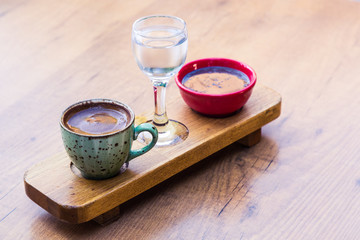 Turkish coffee, a glass of water and a chocolate snack are served on a designer tray on a wooden table. Stylishly decorated service in the cafe and restaurant.