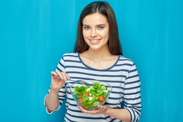 Woman eating salad with fork from glass bowl.