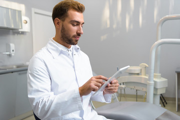 handsome young dentist in coat using tablet in office