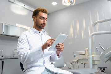 Fototapeta premium bottom view of attractive young dentist in coat using tablet in office
