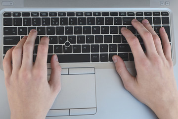 Hands typing keyboard of gray laptop closeup top view.