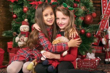 Fototapeta na wymiar Two Girls Under Christmas Tree are Playing with Toys