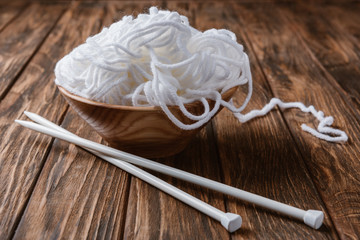 close up view of white yarn in bowl and knitting needles on wooden tabletop