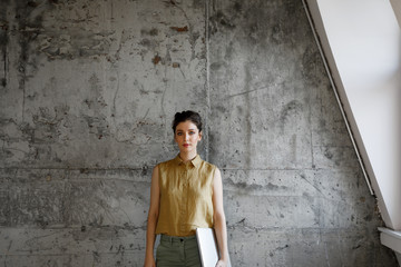 Portrait of beautiful young businesswoman standing at modern industrial office space and looking at camera.