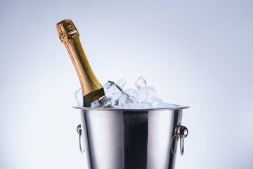 close up view of bottle of champagne in bucket with ice cubes on grey background