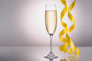 close up view of glass of champagne and yellow confetti on grey background
