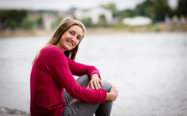 Fototapeta na wymiar Lachende junge Frau sitzt an einem Fluss