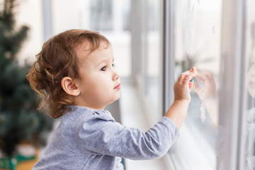 Cute little three years girl looking through window with holiday decoration.