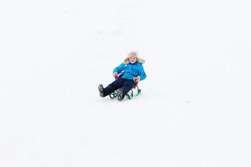 Fototapeta na wymiar winter active fun - happy girl riding a snow hill on a sled