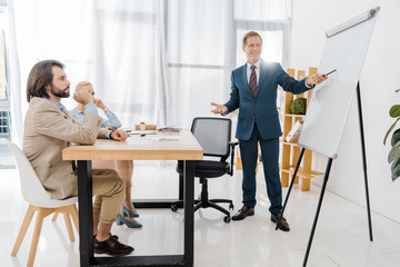 adult businessman talking to couple and pointing at white board in office