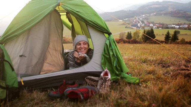 Woman laughing into camera lying in camping tent and enjoy with autumn morning in mountain valley