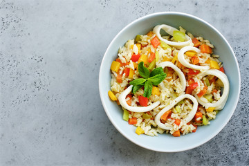 Rice with vegetables and squid rings. Top view, gray concrete background