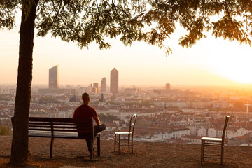 Man on a bench relaxing and enjoying the summer sunrise over a city. Lyon, France.