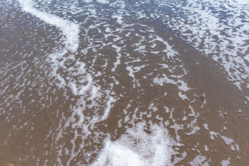 Texture of the remains of a foamy wave on the beach, background