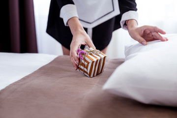 Small gift. Close up of a small present being put on the bed by a female hotel maid in the room