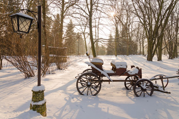 Fototapeta na wymiar A vintage horse carriage and a retro style lantern in the snowy landscape in the forest in the late afternoon before sunset