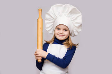 Children cook. Happy little girl in chef uniform holds rolling pin isolated on white background