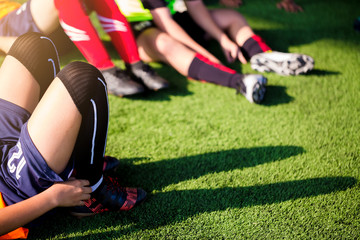 Kid soccer players are sitting with warming on green artificial turf for stretch muscles before and after play soccer game.