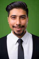 Young bearded Iranian businessman against green background